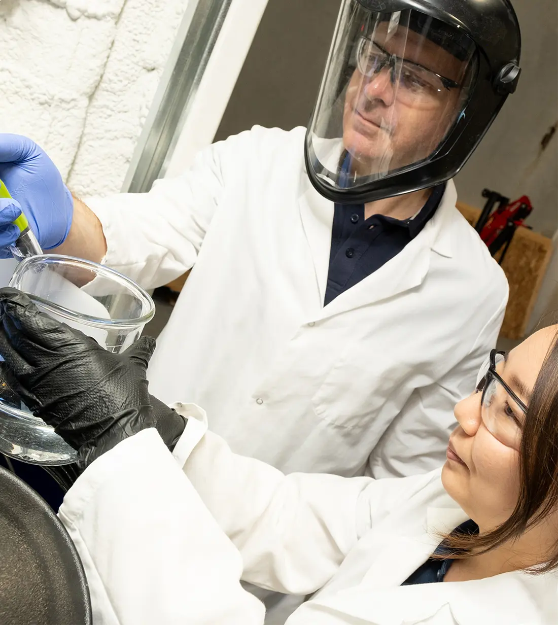 two lab technicians with eye and face protection inspecting a glasss